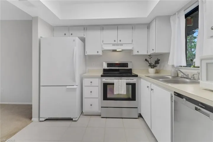 Kitchen with white cabinets, sink, appliances with stainless steel finishes, a tray ceiling, and light carpet