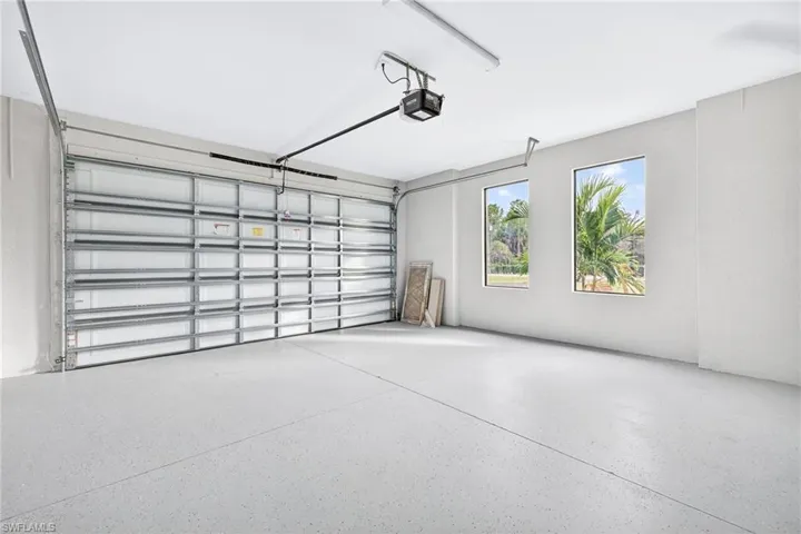 Spacious garage featuring a durable speckled epoxy floor, an automatic overhead door opener, and two windows providing natural light