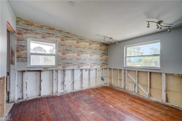 Spare room featuring wooden walls, hardwood / wood-style flooring, rail lighting, and lofted ceiling