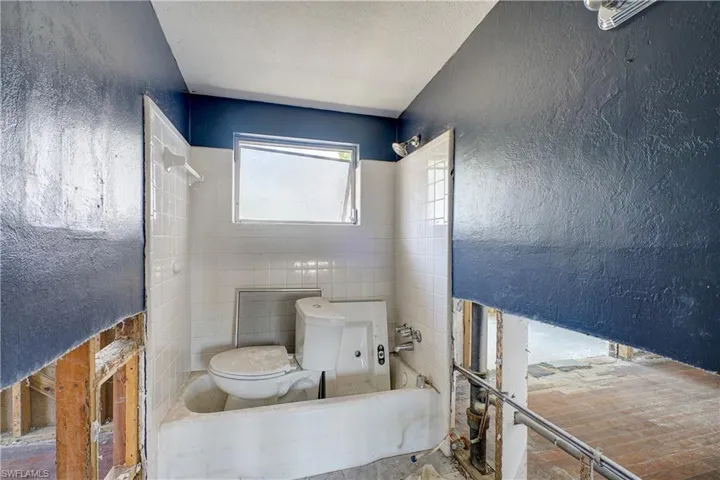 Bathroom with tiled shower / bath, a textured ceiling, toilet, and tile walls