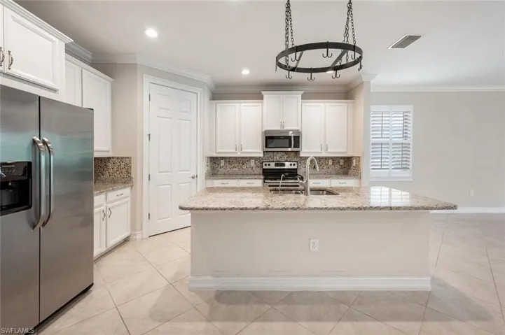 Kitchen with white cabinetry, an island with sink, light stone countertops, and appliances with stainless steel finishes