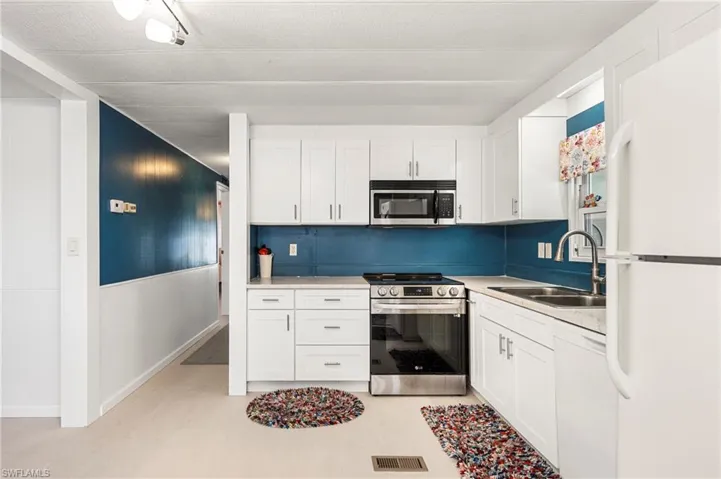 Kitchen featuring stainless steel appliances, white cabinetry, and light countertops