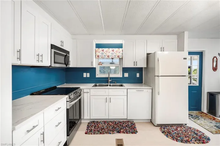 Kitchen featuring stainless steel appliances, white cabinets, a textured ceiling, and light stone counters