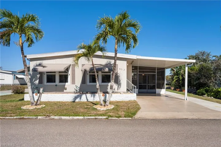Manufactured / mobile home with a carport, concrete driveway, a sunroom, and a front lawn