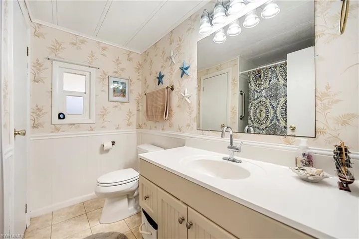 Bathroom with wainscoting, vanity, a shower with shower curtain, light tile patterned floors, and wallpapered walls