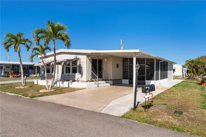 Manufactured / mobile home featuring a carport, a front lawn, concrete driveway, and a sunroom