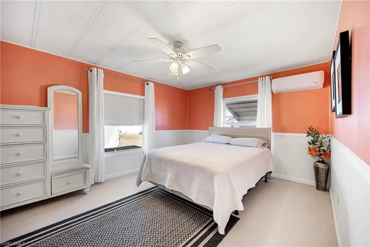 Bedroom with multiple windows, a ceiling fan, a wall mounted air conditioner, wood walls, and wainscoting