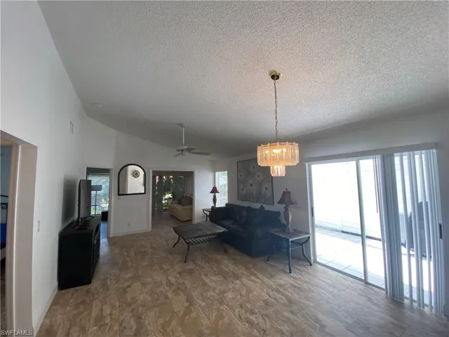 Living area with a textured ceiling, a chandelier, a ceiling fan, and high vaulted ceiling