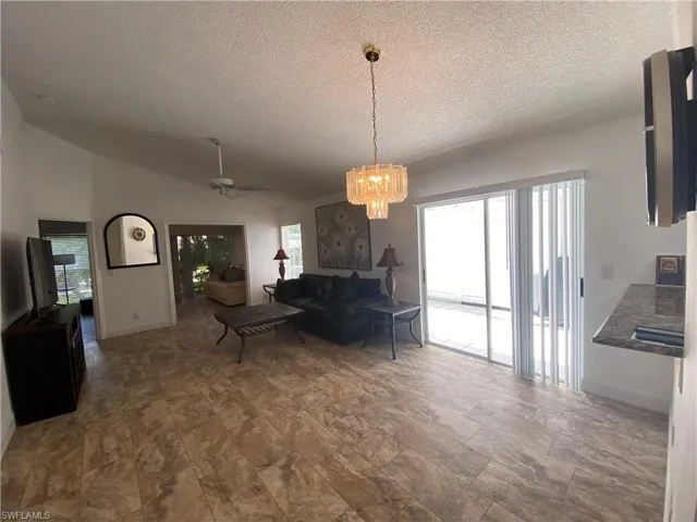 Living room featuring a textured ceiling, vaulted ceiling, ceiling fan, and a chandelier