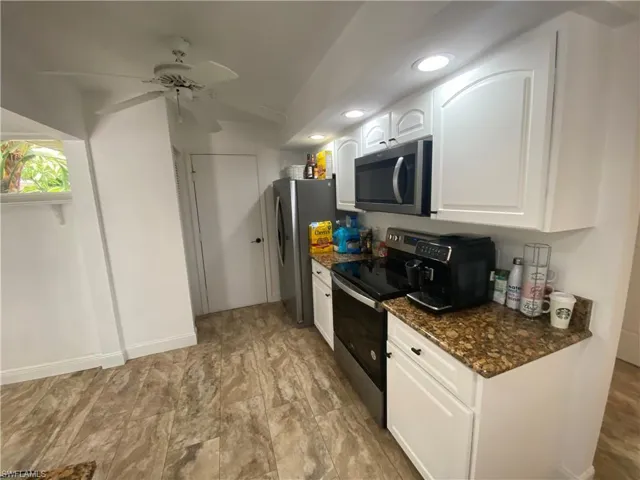 Kitchen with stainless steel appliances, white cabinets, ceiling fan, dark stone countertops, and recessed lighting