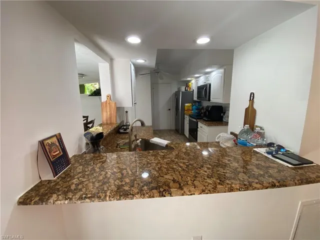 Kitchen with a peninsula, black range with electric cooktop, white cabinetry, dark stone countertops, and recessed lighting