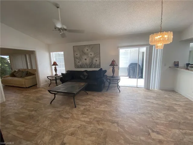 Living area with a textured ceiling, a chandelier, ceiling fan, and vaulted ceiling