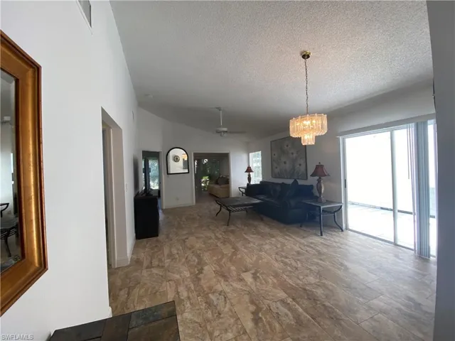 Living room with vaulted ceiling, a textured ceiling, a chandelier, and ceiling fan