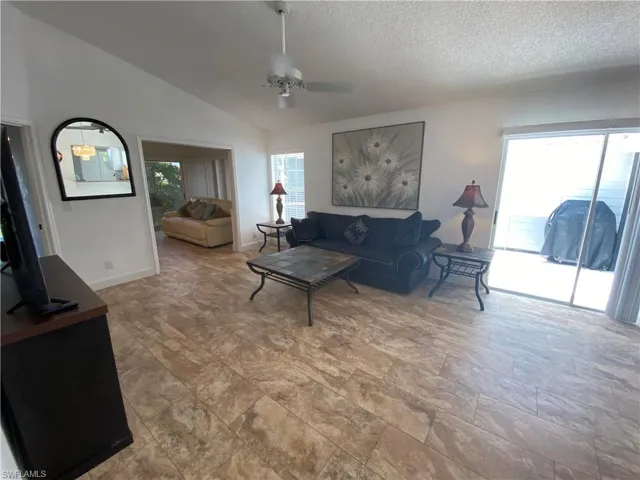 Living room with vaulted ceiling, ceiling fan, and a textured ceiling