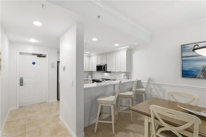 Kitchen with light countertops, a breakfast bar area, white cabinets, stainless steel microwave, and recessed lighting