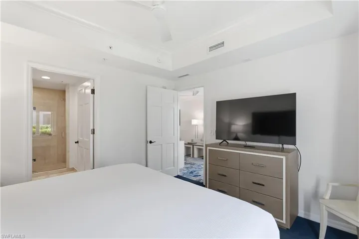 Bedroom with ornamental molding, connected bathroom, and a tray ceiling