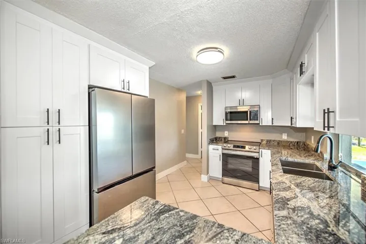 Kitchen featuring appliances with stainless steel finishes, white cabinetry, dark stone countertops, and sink