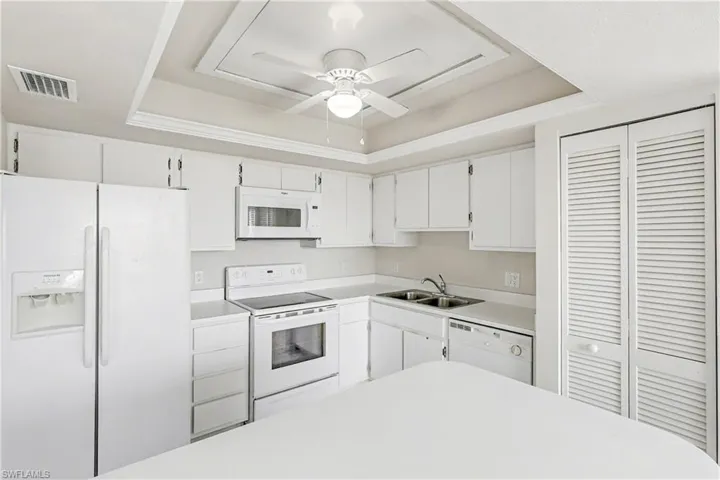 Kitchen with a raised ceiling, white appliances, light countertops, and white cabinets