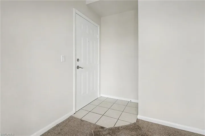 Empty room with light tile patterned floors and light colored carpet