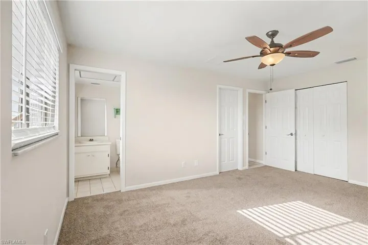 Unfurnished bedroom featuring light carpet, a ceiling fan, ensuite bathroom, and a closet