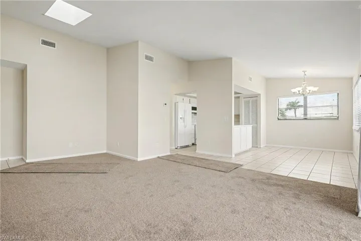 Unfurnished room with light colored carpet, a chandelier, a skylight, and light tile patterned floors