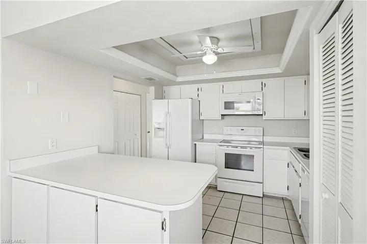 Kitchen featuring white appliances, a raised ceiling, light countertops, white cabinetry, and a peninsula