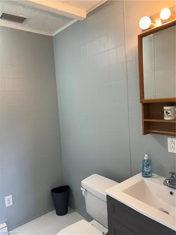 Bathroom featuring a textured ceiling, vanity, tile walls, toilet, and tile patterned floors