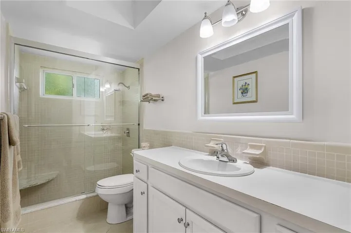 Bathroom featuring toilet, a shower with door, vanity, decorative backsplash, and tile walls