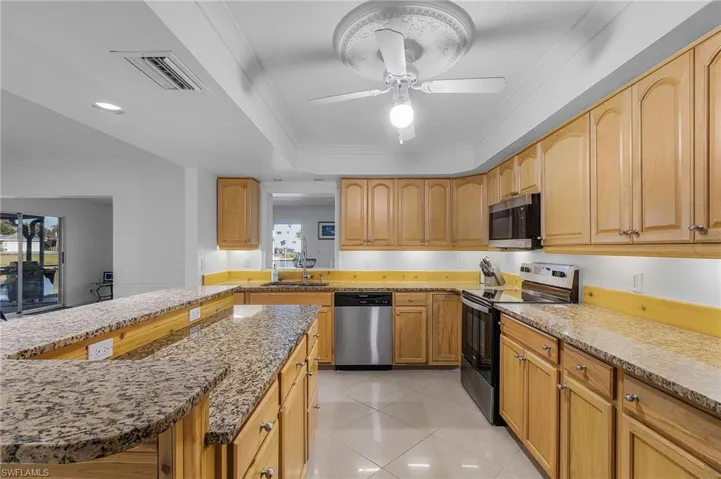 Kitchen featuring light tile patterned floors, sink, light stone countertops, ceiling fan, and appliances with stainless steel finishes