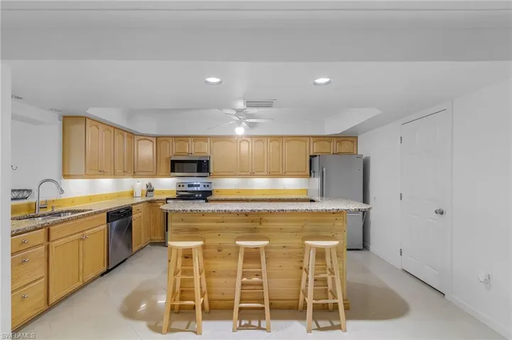 Kitchen featuring appliances with stainless steel finishes, a center island, sink, ceiling fan, and light stone counters