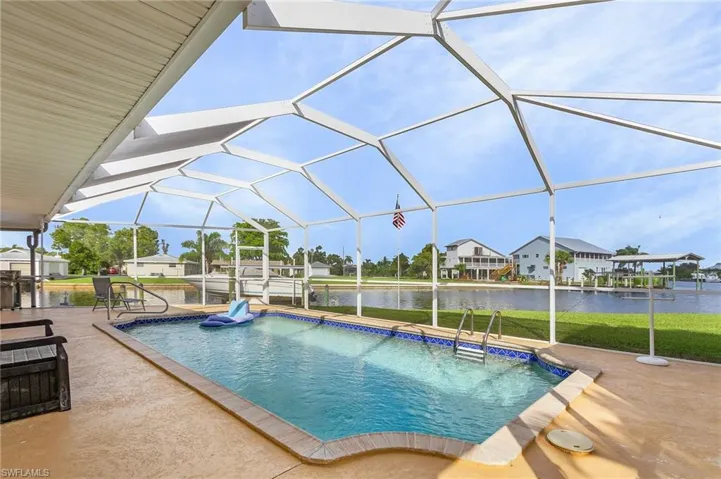 View of pool featuring a water view, a lawn, a patio, and glass enclosure