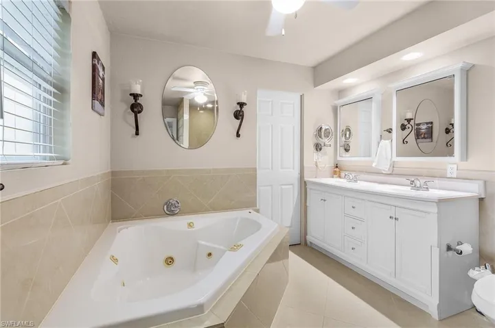 Bathroom with tiled tub, vanity, ceiling fan, and tile patterned floors