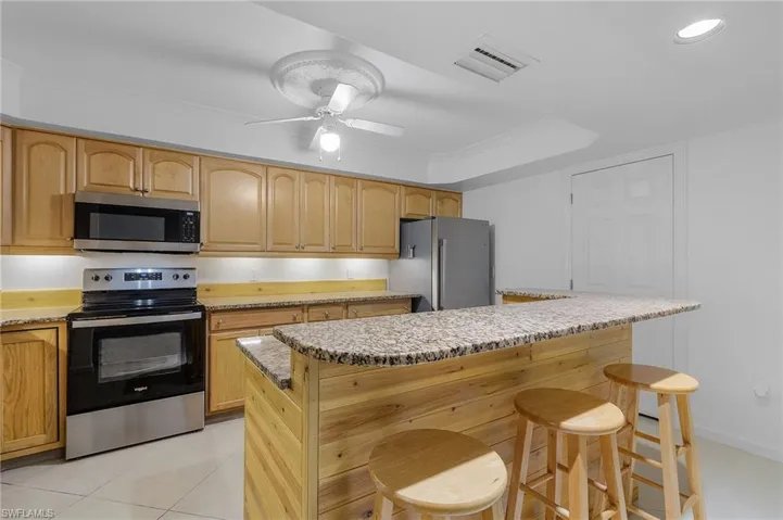 Kitchen featuring appliances with stainless steel finishes, a center island, a breakfast bar, ceiling fan, and light tile patterned flooring