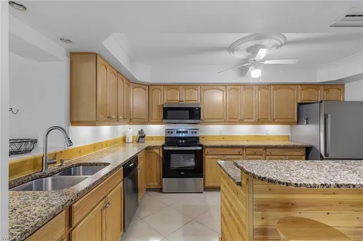 Kitchen with light stone countertops, stainless steel appliances, ornamental molding, sink, and ceiling fan