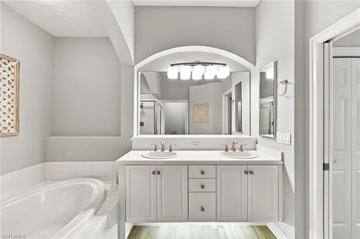 Dual vanity with white cabinetry and integrated sinks, complemented by a large arched mirror and modern light fixture