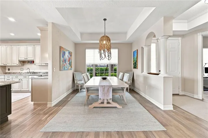 Tray ceiling with a central pendant fixture, wood-finish flooring, and arched architectural details