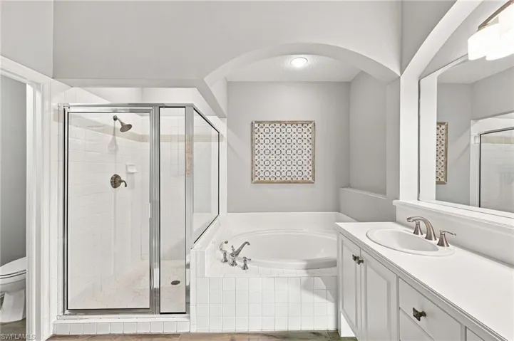 Alcove soaking tub with tiled surround, walk-in shower with glass enclosure, single vanity with white countertop, and brushed nickel fixtures