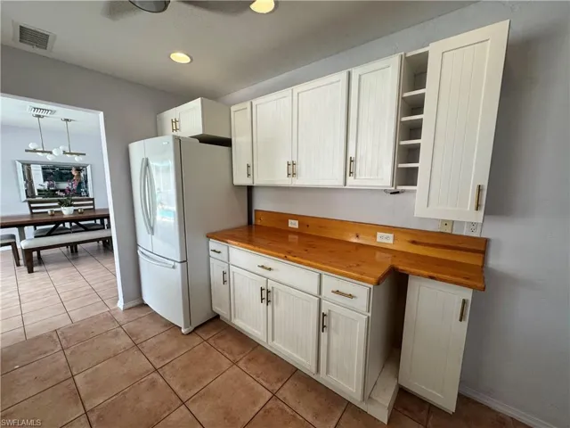 Kitchen with light tile patterned flooring, freestanding refrigerator, visible vents, open shelves, and wood counters