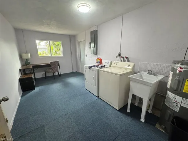 Washroom featuring electric water heater, a sink, electric panel, washing machine and dryer, and laundry area
