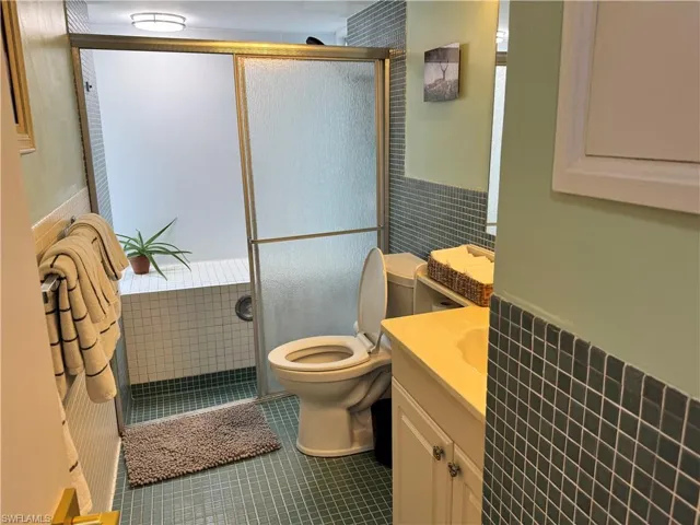 Bathroom featuring wainscoting, tile patterned floors, a shower stall, and toilet