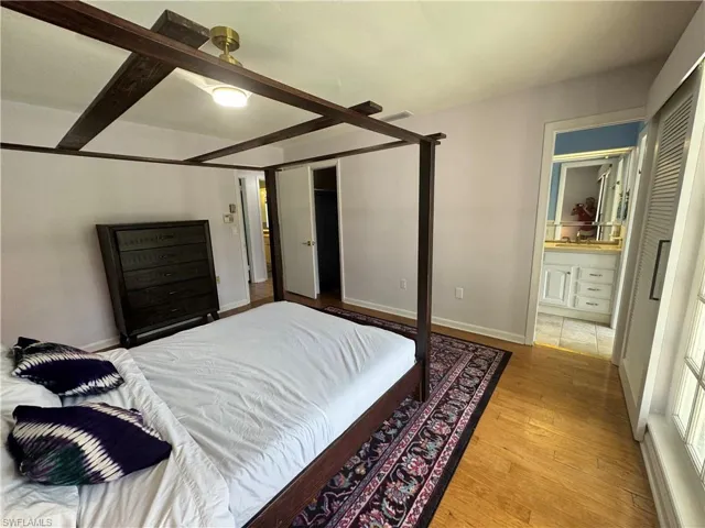 Bedroom with baseboards, beamed ceiling, light wood finished floors, ensuite bath, and visible vents