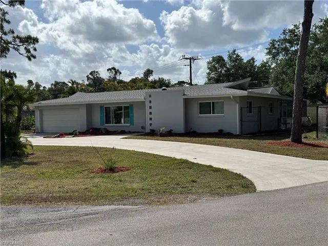Ranch-style home with curved driveway, an attached garage, fence, a front yard, and stucco siding