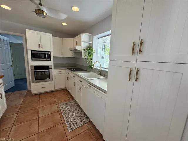 Kitchen featuring under cabinet range hood, light countertops, a sink, appliances with stainless steel finishes, and white cabinetry