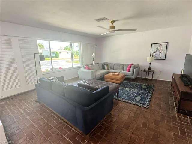 Living area featuring a ceiling fan, visible vents, and brick floor