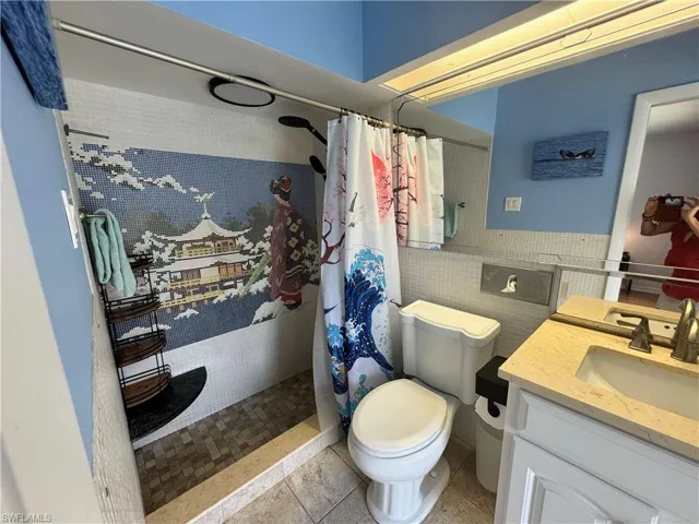 Bathroom with tile patterned flooring, toilet, vanity, tile walls, and tiled shower