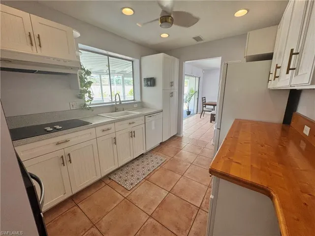 Kitchen with a sink, butcher block countertops, white cabinetry, white appliances, and under cabinet range hood