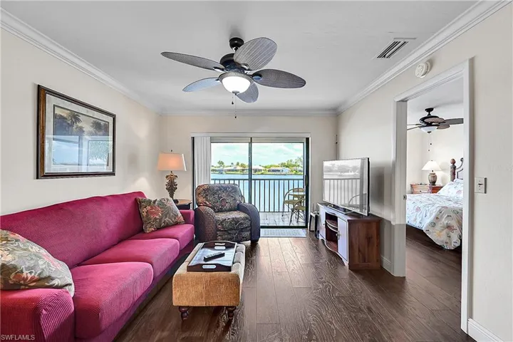 Living area with ceiling fan, dark wood-style flooring, baseboards, and ornamental molding
