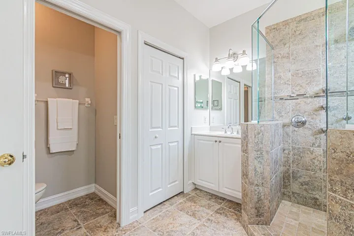 Full bathroom with tiled shower, vanity, baseboards, and toilet