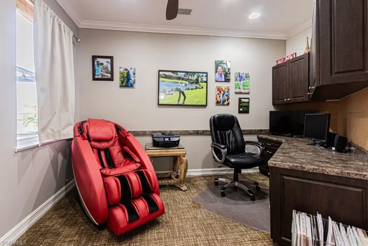 Home office featuring baseboards, crown molding, visible vents, dark carpet, and ceiling fan