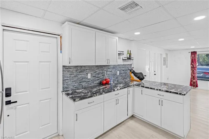 Kitchen with dark stone countertops, tasteful backsplash, a peninsula, white cabinetry, and a drop ceiling